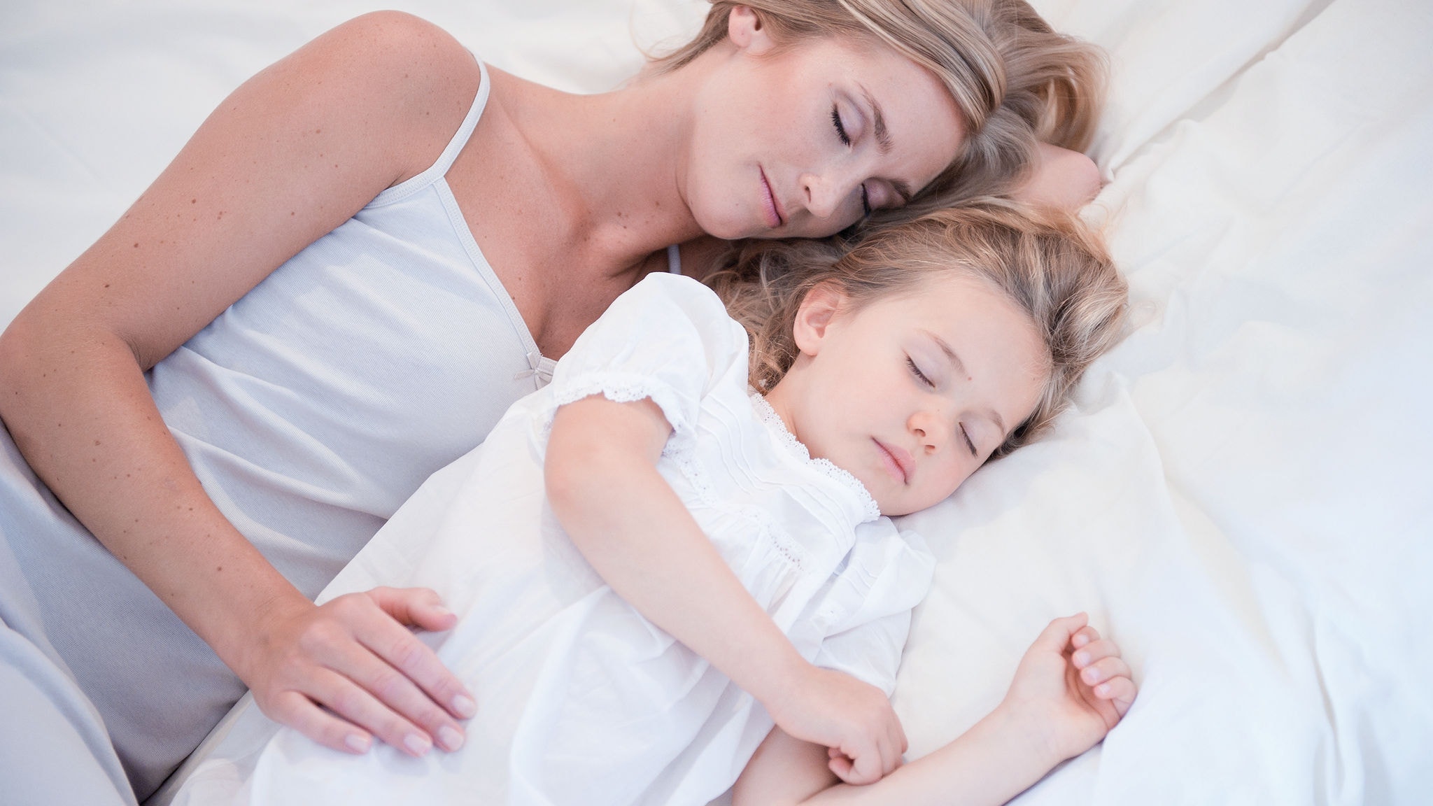 Maminka a malá dcerka spí vedle sebe v bílé posteli v čistém vzduchu