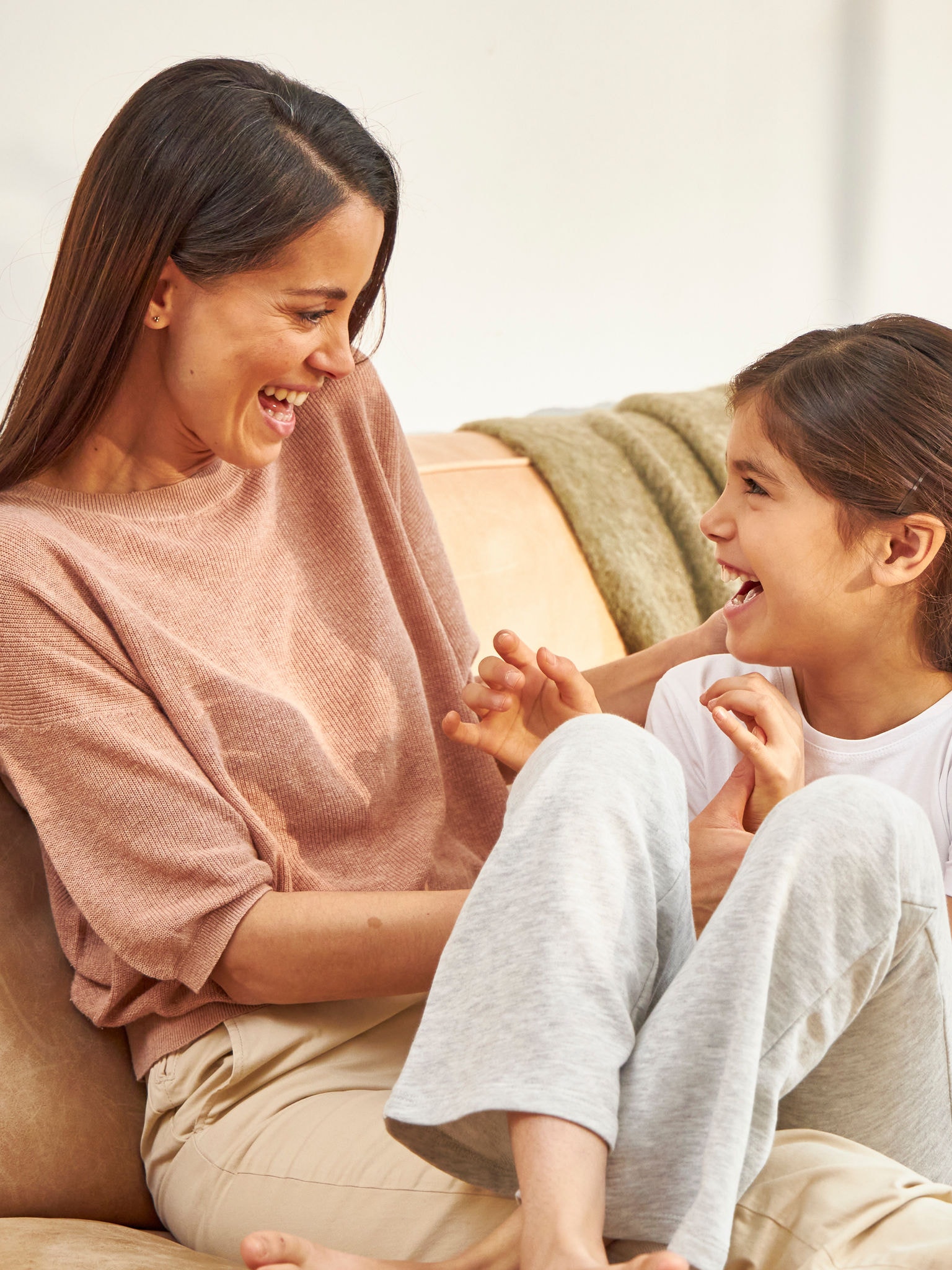 Matka se mazlí s dcerou, zatímco se obě smějí na gauči